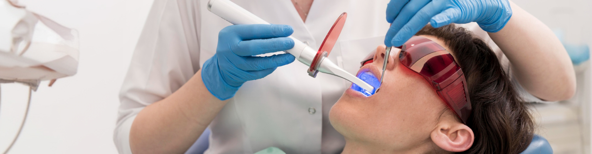 Patient wearing protective glasses while receiving an in-office teeth whitening treatment with a dental curing light.